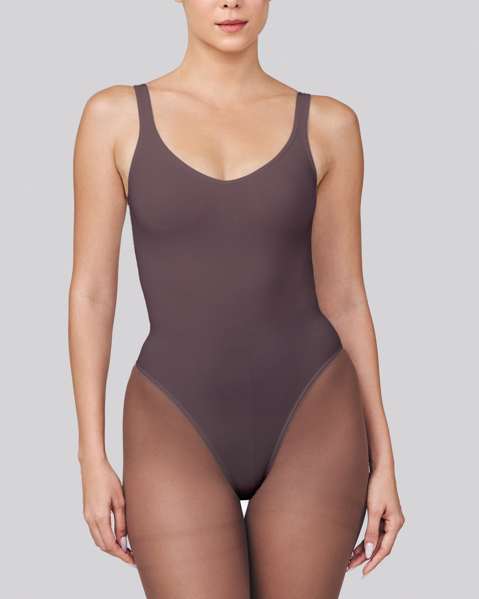 Woman wearing a dark brown bodysuit on a light gray background