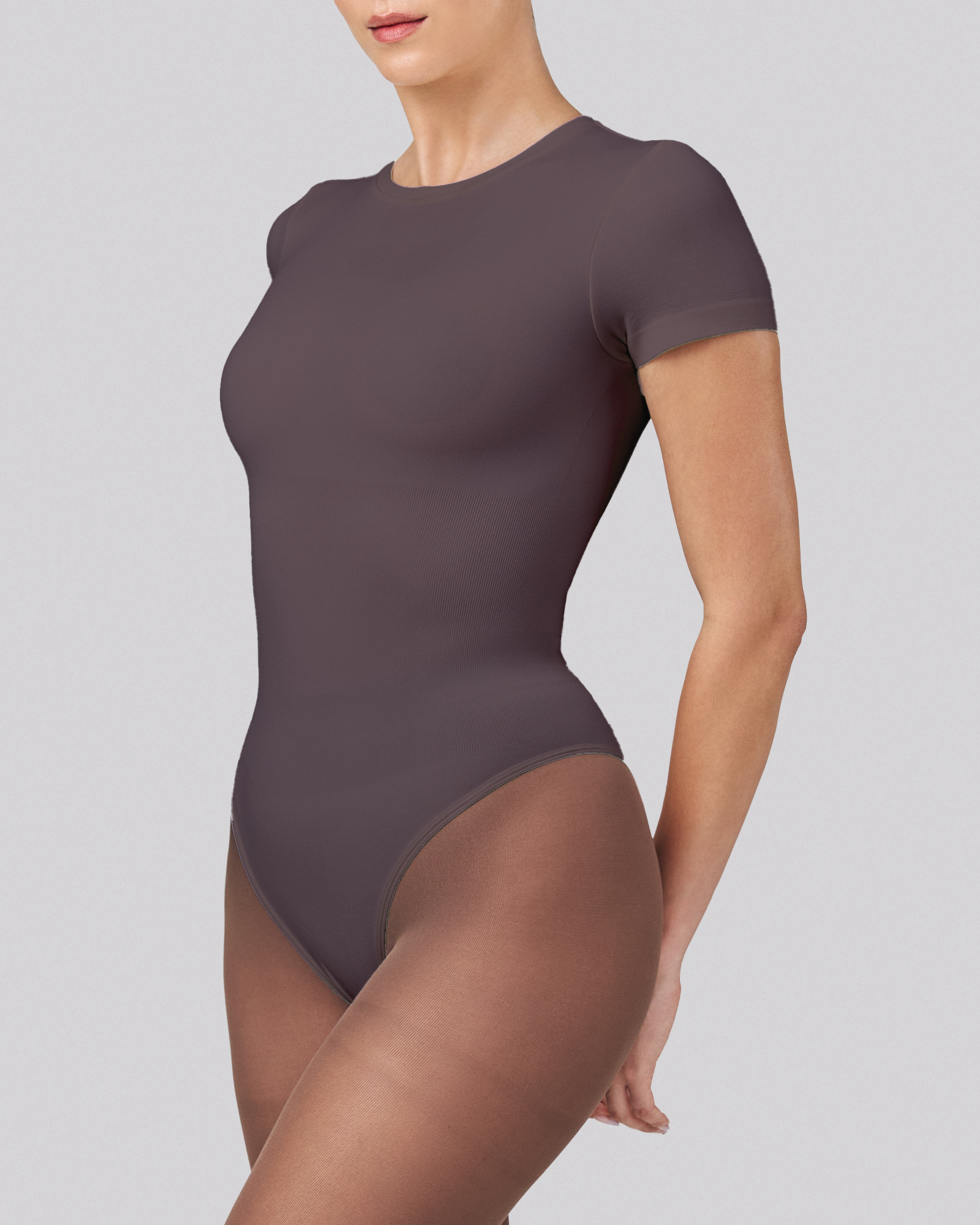 Person wearing a dark gray bodysuit on a light gray background