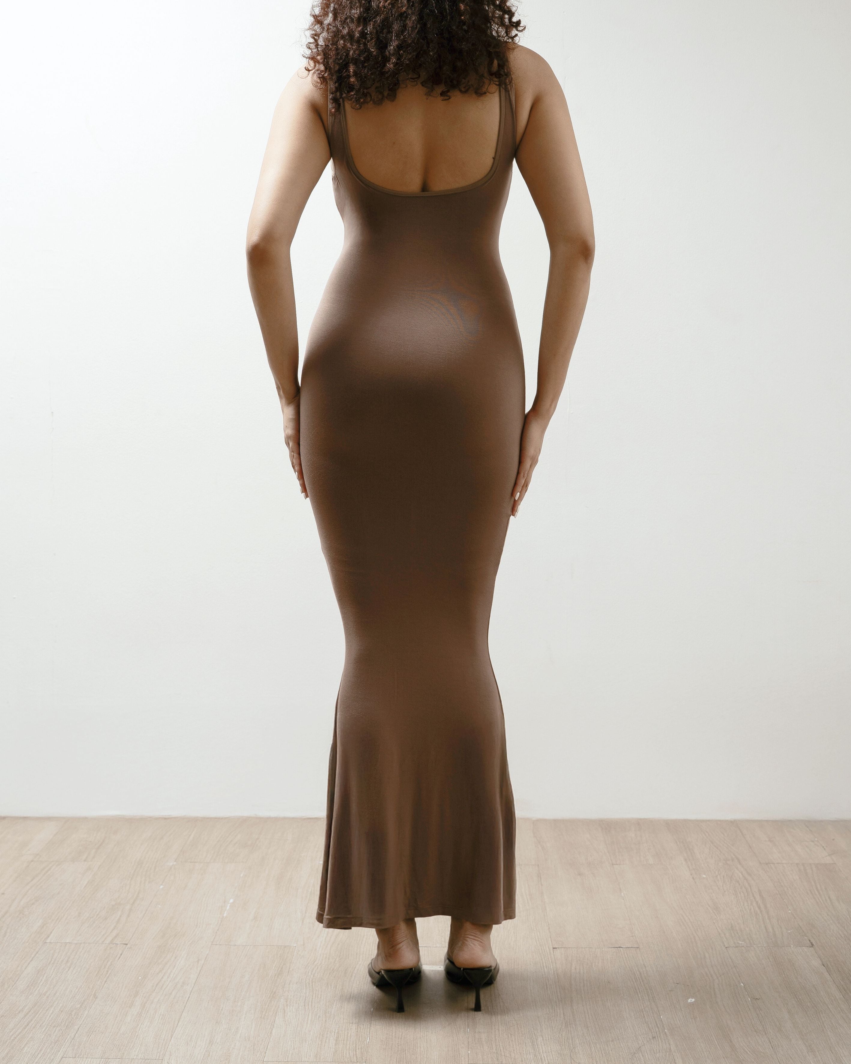 Woman wearing a brown dress against a white wall.